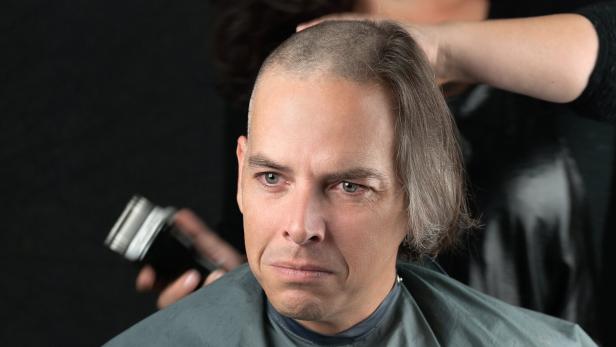 Ein trauriger Mann, dem für eine Krebs-Spendenaktion die langen Haare abrasiert werden.