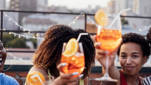Freunde - offenbar in einer Rooftop-Bar - prosten einander mit Aperol Spritz zu.