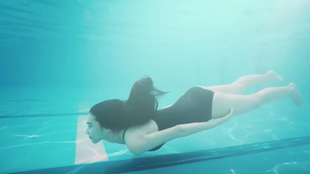 Eine Frau mit dunklen Haaren schwimmt unter Wasser.