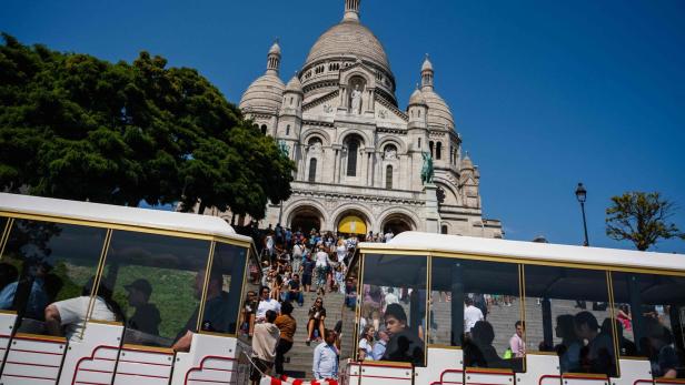 Die Basilika Sacré-Cœur de Montmartre in Paris, mit Touristen auf den Stufen und einem Touristenzug im Vordergrund.