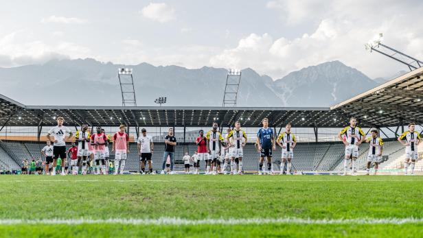 Eine Fußballmannschaft steht auf dem Rasen vor einem Stadion und Bergen.