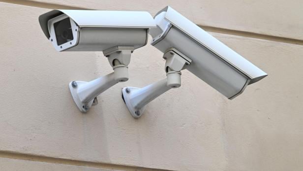 Zwei weiße Überwachungskameras sind an einer Wand montiert.