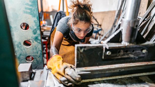 Young Woman Bending Metal On Machine In A Workshop