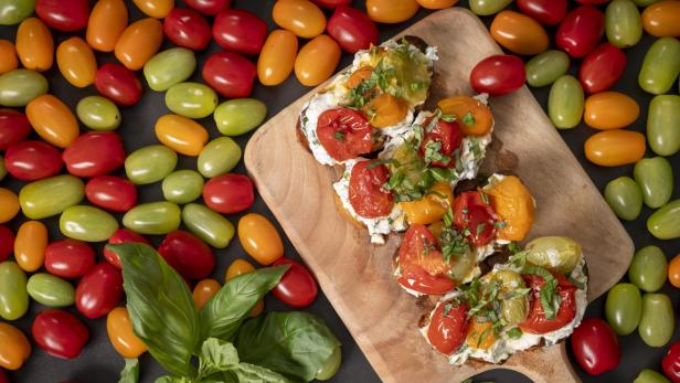 Ein Holzschneidebrett mit einer Ansammlung von Tomaten und frischen Kräutern.