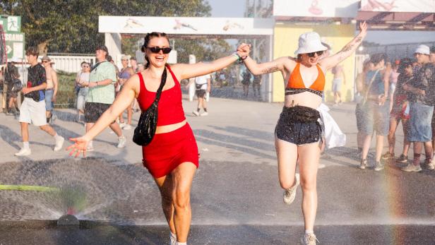 2 Frauen tanzen ausgelassen vor einem Wassersprenger