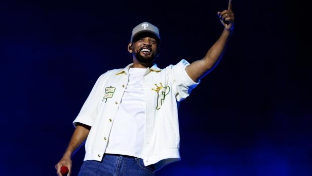 Will Smith steht auf einer Bühne und zeigt mit dem Finger nach oben.