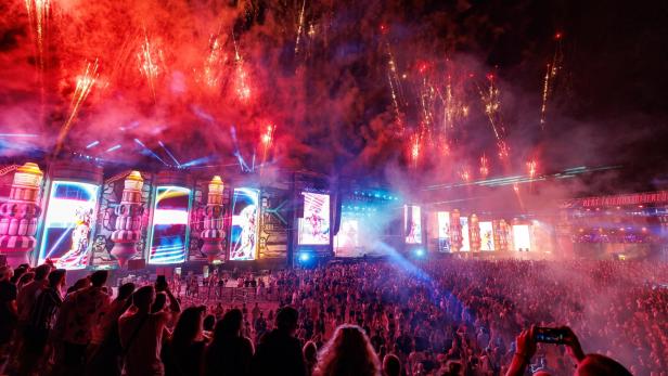 Eine große Menschenmenge genießt ein Konzert mit Feuerwerk im Hintergrund.