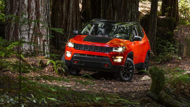 Ein orangefarbener Jeep Compass fährt durch einen Wald.