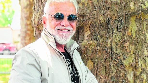 Nino de Angelo Nino de Angelo mit Tätowierungen lehnt an einem Baum und lächelt.