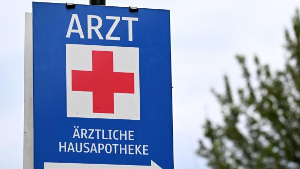Blaues Schild mit rotem Kreuz, der Aufschrift „Arzt“ und einem weißen Pfeil nach rechts.