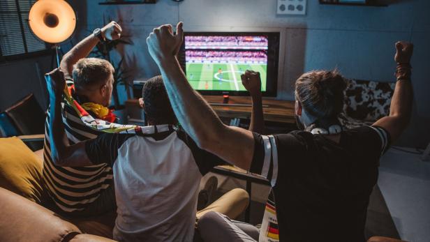 Fußballfans sitzen gemeinsam vor dem Fernseher und jubeln.