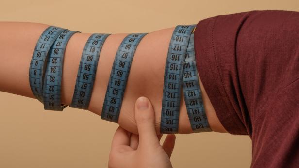 Eine Frau misst ihren Oberarmumfang mit einem Maßband.