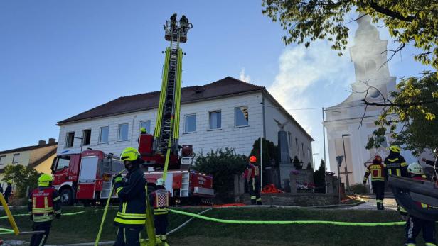 Aufnahmen von einem Haus, aus dem Rauch dringt. Im Vordergrund ist die Feuerwehr bei ihren Löscharbeiten zu sehen.