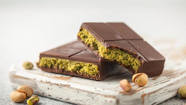 Zwei Stücke Dubai-Schokolade mit Pistazienfüllung auf einem Holzbrett.