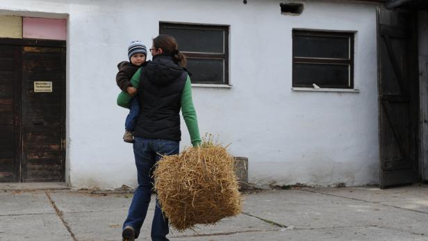 Landwirtin mit Strohballen in der Hand und Kleinkind im Arm.
