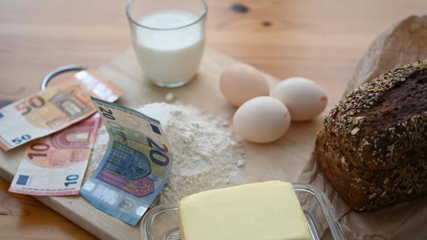 Symbolbild: Geldscheine, die neben Lebensmitteln - unter anderem Eier, Butter und Brot - liegen.