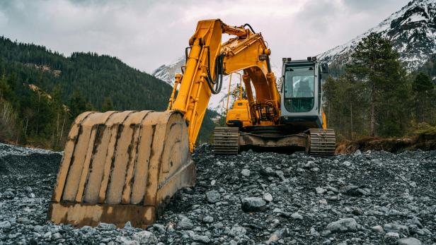 Gelber Bagger setzt Schaufel im Gestein an