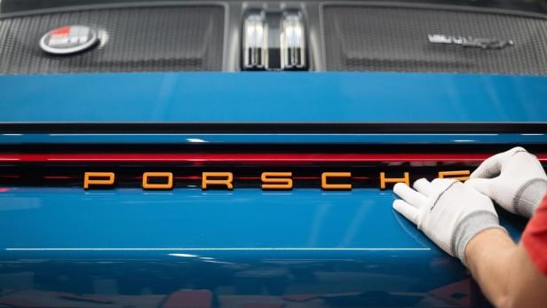 Ein Arbeiter bringt den Schriftzug „Porsche“ an einem blauen Auto an.