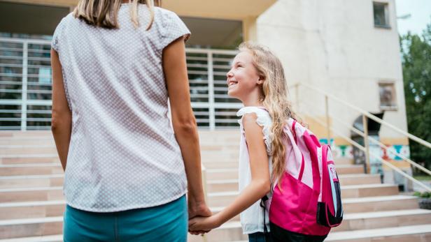 Eine Mutter hält die Hand ihrer Tochter vor einer Schule.