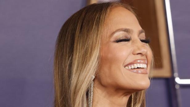 Jennifer Lopez lächelt und trägt ein trägerloses Kleid mit goldenen Akzenten.