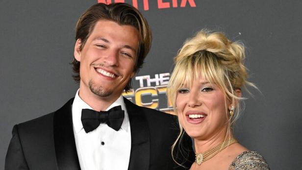 Schauspielerin Millie Bobby Brown und ihr Mann Jake Bongiovi lächeln in die Kamera. Sie tragen elegante Abendkleidung.
