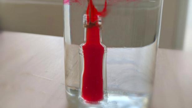 Kleines Gefäß in einem Glas, gefüllt mit rot gefärbter Flüssigkeit. 