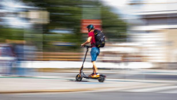 Ein Mann mit Rucksack fährt mit einem Elektroroller über einen Zebrastreifen.
