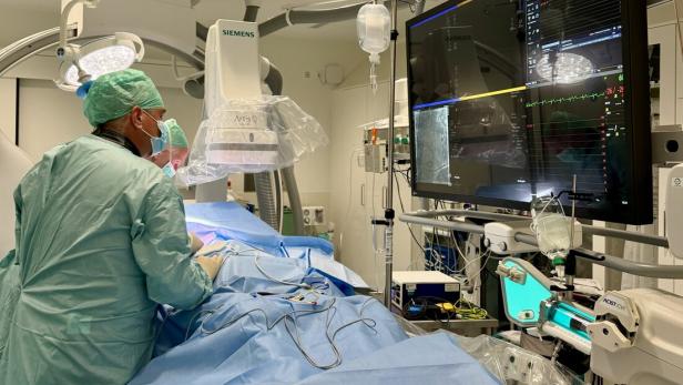 Ein Operationssaal, ein Arzt blickt auf zahlreiche Monitore mit Gesundheitsdaten eines Patienten