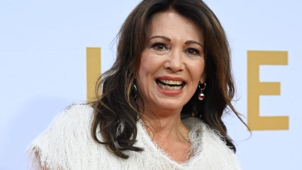 Eine Frau mit weißem Kleid und silberner Handtasche lächelt.