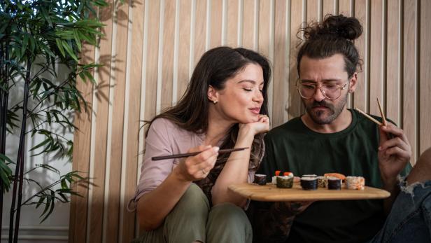 Ein junges Paar isst Sushi, die Frau möchte vom Teller des Mannes naschen