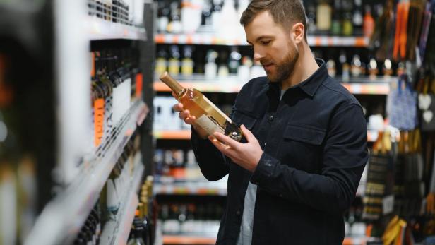 Mann in einem Supermarkt, liest das Etikett einer Weinflasche in seinen Händen