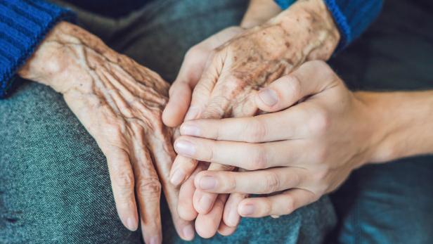 Eine junge Hand berührt die Hände einer alten Person.