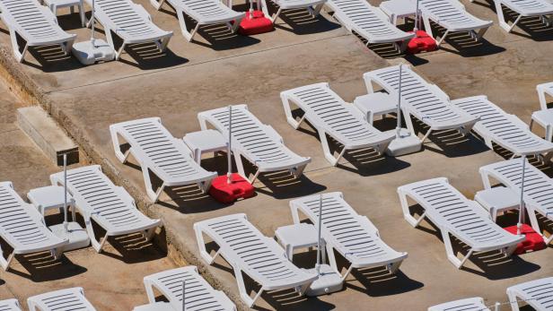 Weiße Sonnenliegen stehen aneinandergereiht am Strand