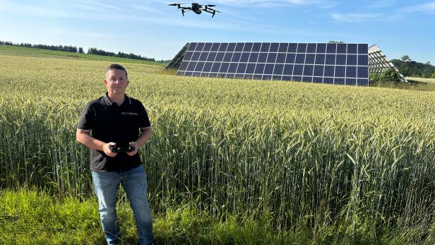Ein Mann steht mit einem Controller vor einem Feld, im Hintergrund Solarpanele.