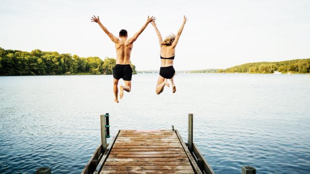 Two Friends Jumping Off Jetty At Lake Together