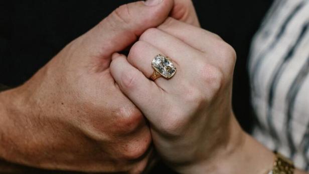 Ein Paar hält Händchen, wobei ein großer Diamantring an der Hand der Frau zu sehen ist.