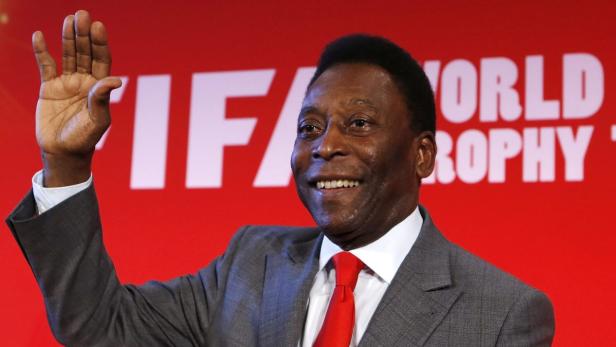 Pelé lächelt und winkt vor einem roten FIFA-Hintergrund.