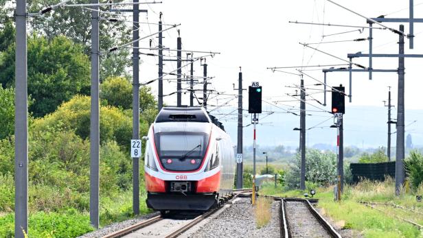 ÖBB-Zug fährt auf elektrifizierter Strecke mit Oberleitungen und Signalen durch eine grüne Landschaft.