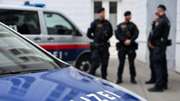 Polizeiautos, drei Polizisten im Hintergrund.