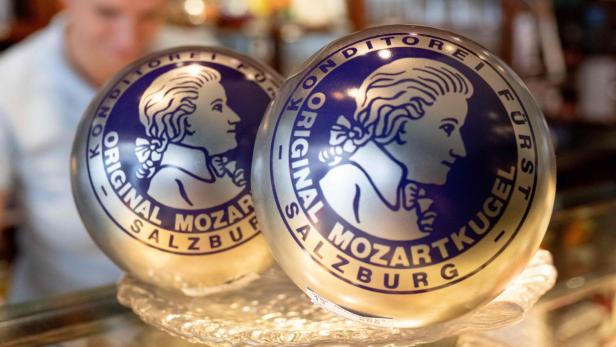 Zwei Kugeln mit Mozartkugel-Logo in einer Vitrine, im Hintergrund eine unscharfe Person.
