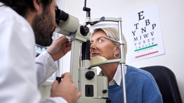 Optiker kontrolliert Augen einer Patientin mit einem Messgerät.