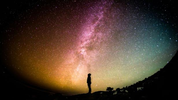 Eine Person blickt auf einen farbenfrohen Himmel, der mit verschiedenen Farbtönen und Sternen gefüllt ist.
