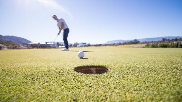 Golfer about to put a ball into the hole on a green on a golf course in South Africa Mann spielt Golf.