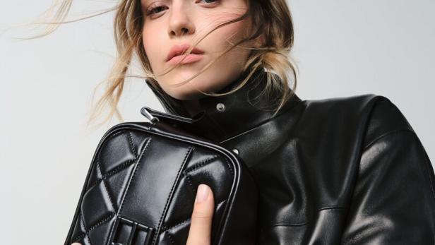 Eine Frau mit Lederjacke hält eine schwarze, gesteppte Handtasche.