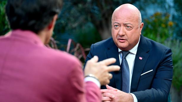 ORF SOMMERGESPRÄCH: WEBHOFER / STOCKER Bundeskanzler Stocker sitzt an einem Tisch. Unscharf im Vordergrund der ORF-Moderator.