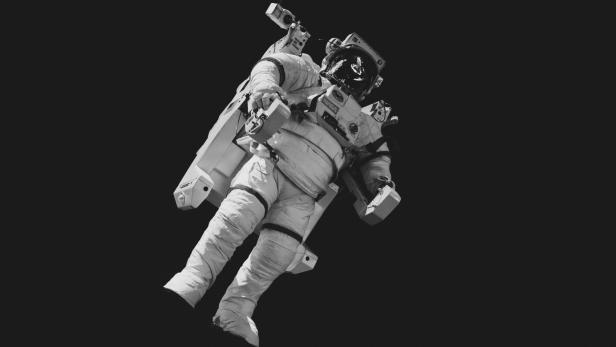Ein Astronaut schwebt im All mit angelegtem Rucksack gegen schwarzen Hintergrund.