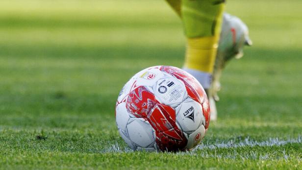Fußball am Rasen, dahinter die Beine eines Spielers
