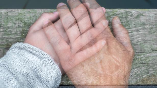 Semi-transparent man's hand on a woman's hand as a sign of farewell by separation or death Eine Hand berührt eine andere.