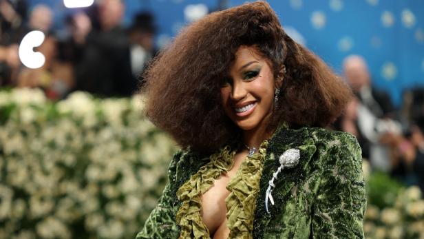 Cardi B lächelt mit voluminöser Frisur in einem grünen Samtoberteil mit Rüschen.