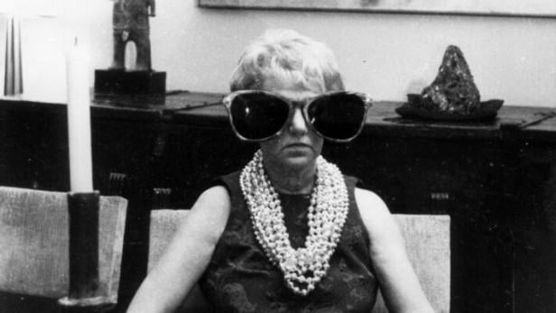 Peggy Guggenheim / Foto Peggy Guggenheim sitzt an einem Schreibtisch. Sie trägt eine übergroße Sonnenbrille.
